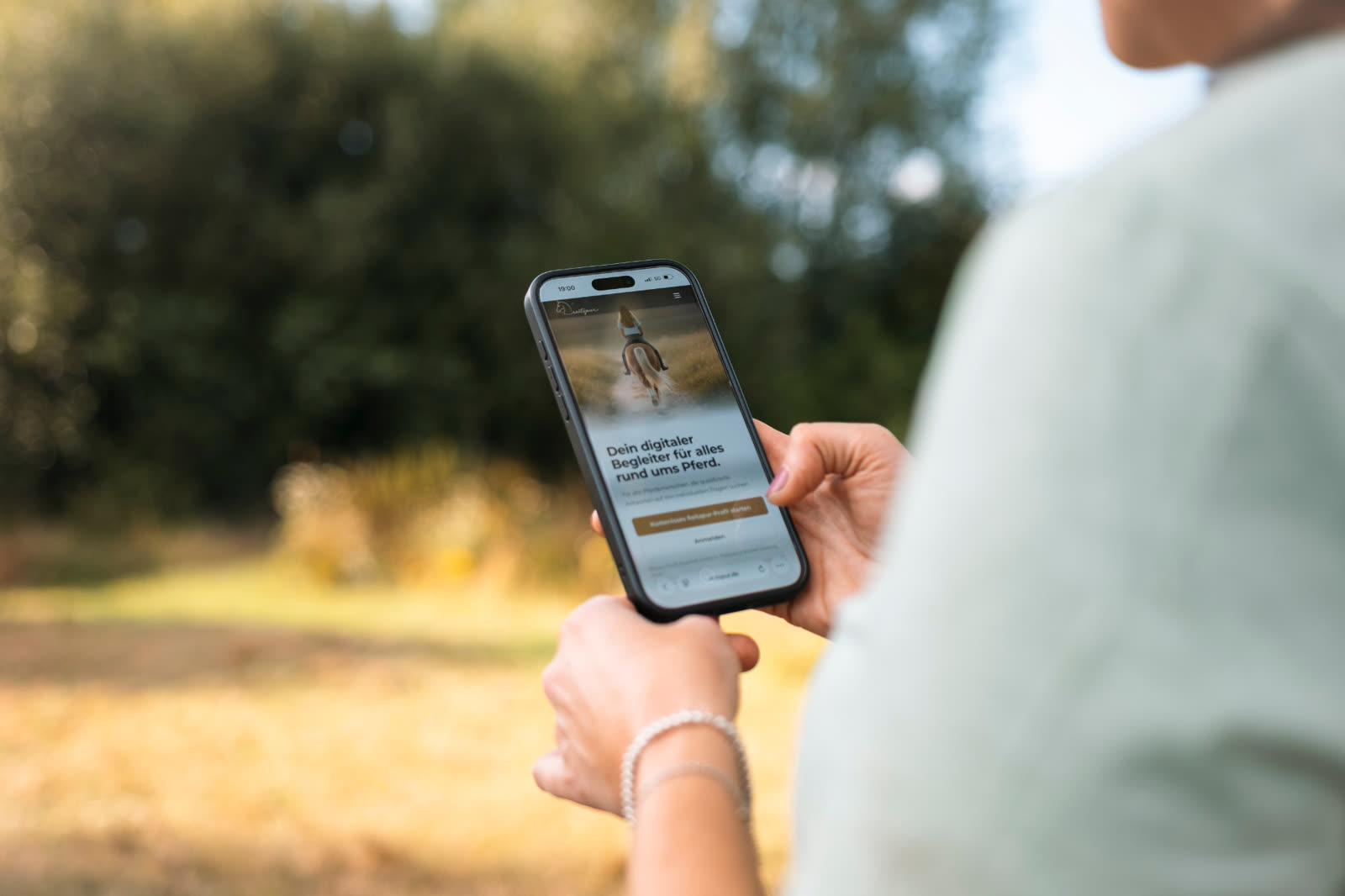 Reiterin hält ihr Smartphone mit geöffneter Reitspur-App auf der Weide